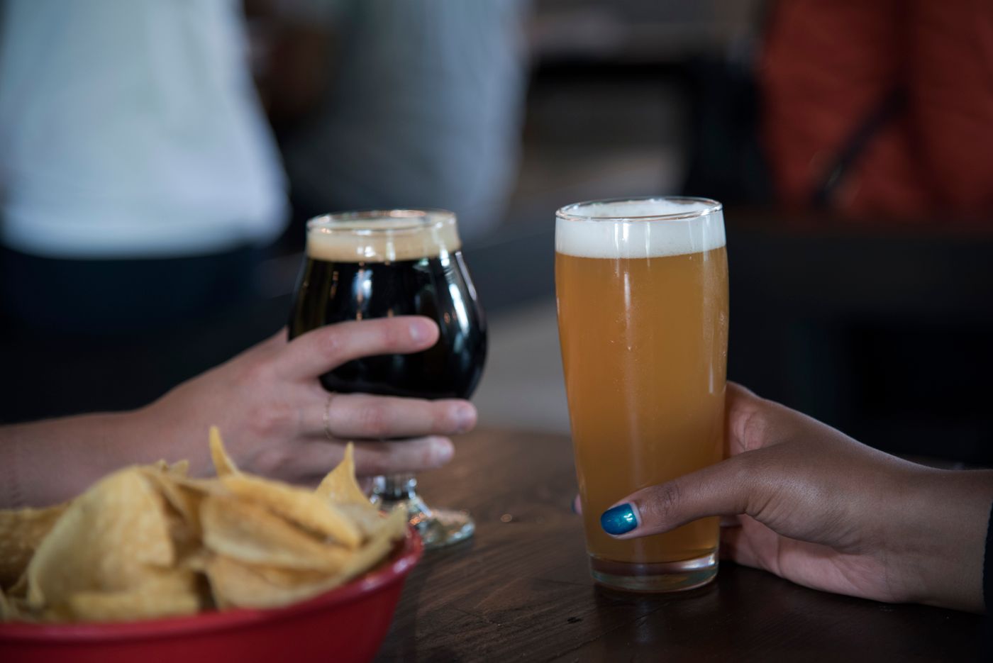 A tall hazy wheat beer beside a dark stout, chips on the table
