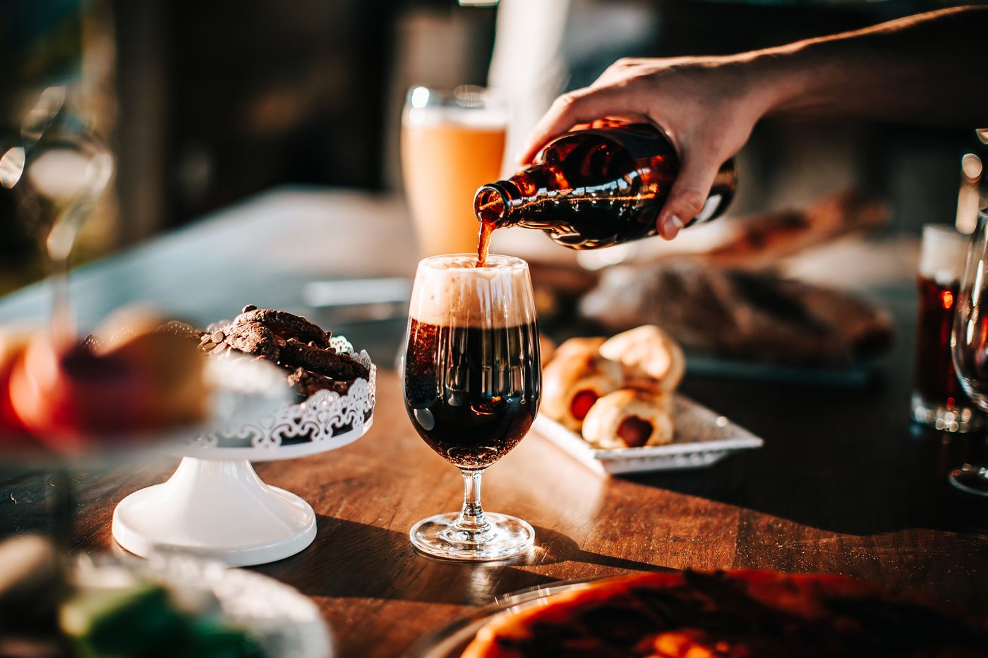 Dark stout poured into a stemmed glass beside pastries and bread