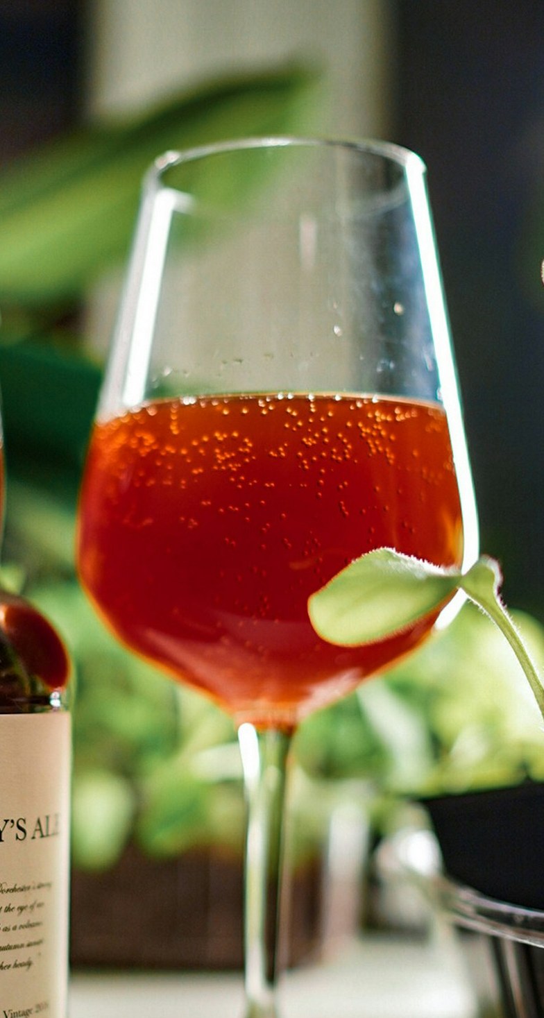 A wine glass of deep red-amber ale with a green leaf in front