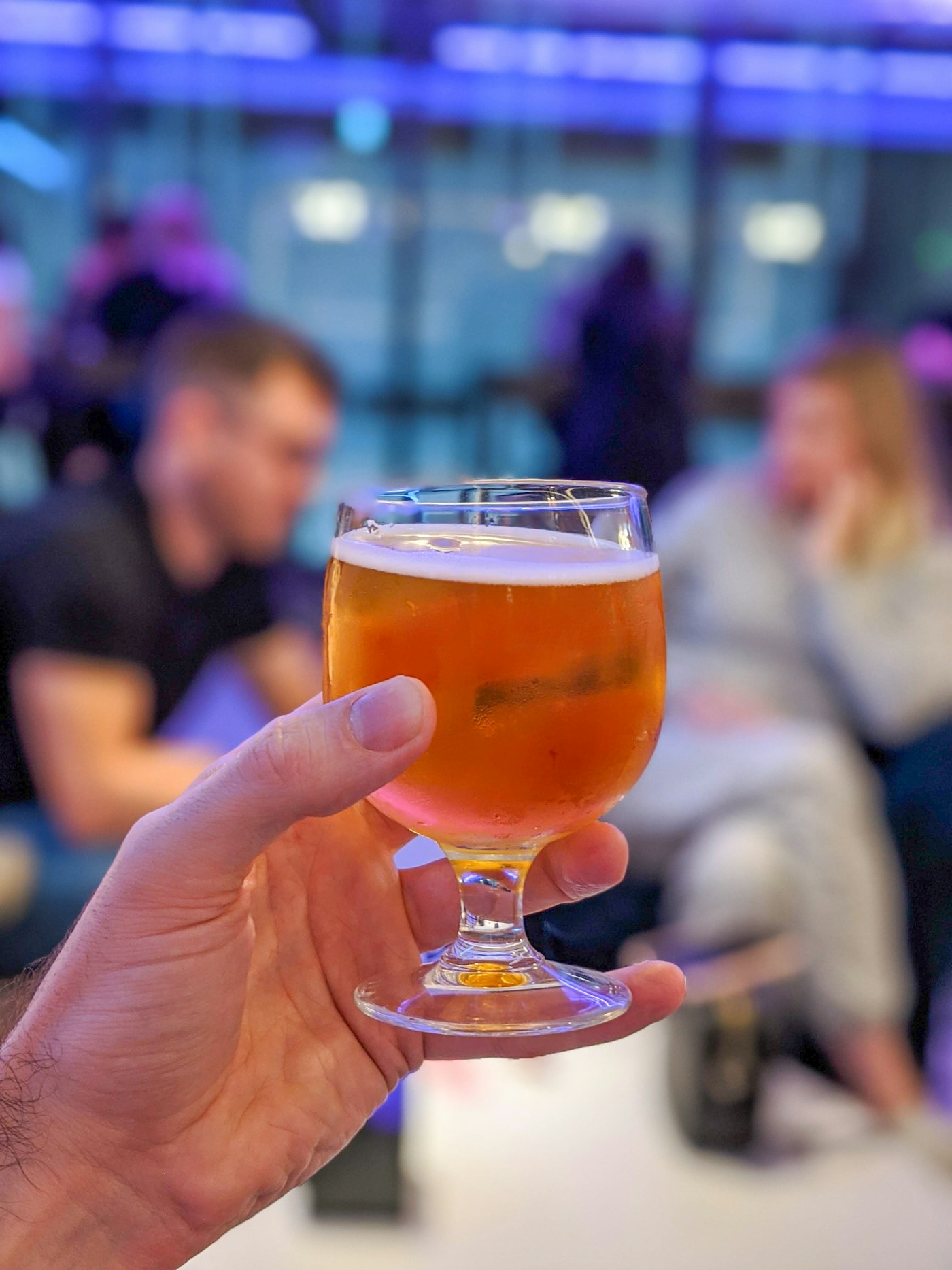 A small stemmed glass of hazy orange beer held toward the camera