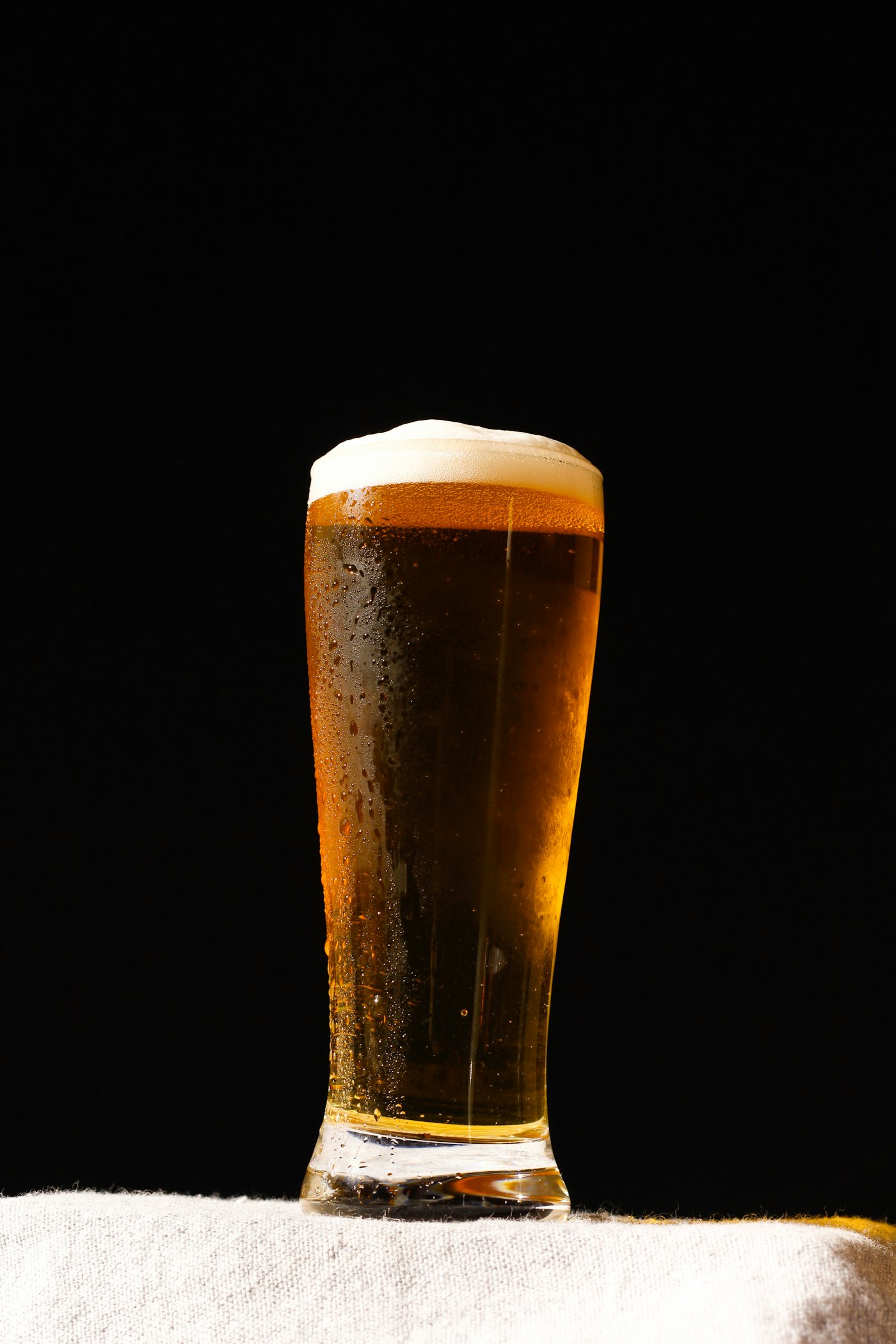 A tall gold lager in a pilsner glass against black