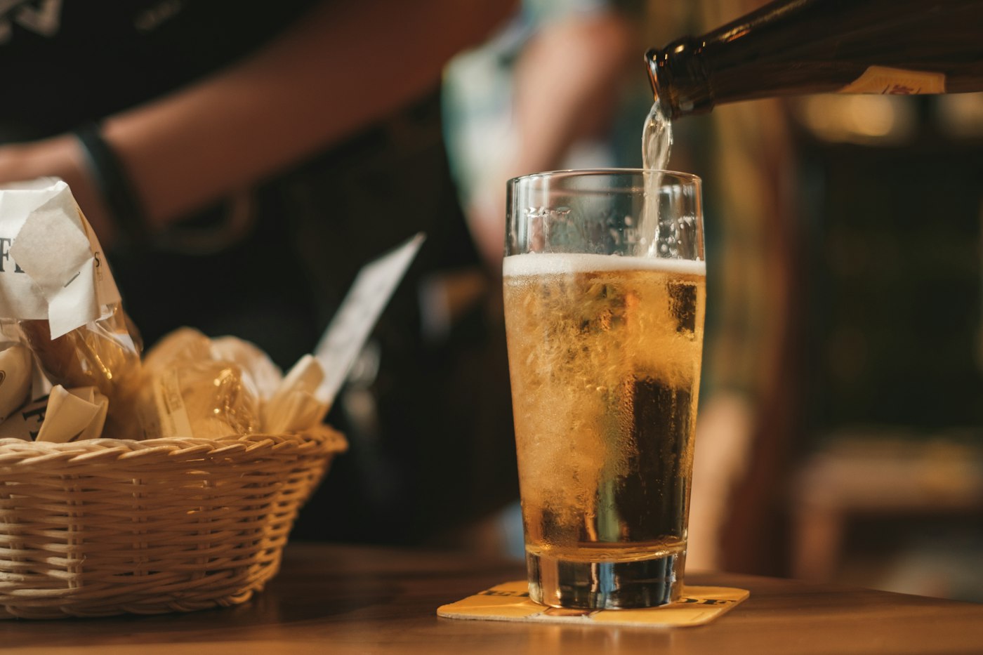 Pale beer poured into a glass next to a basket of bread
