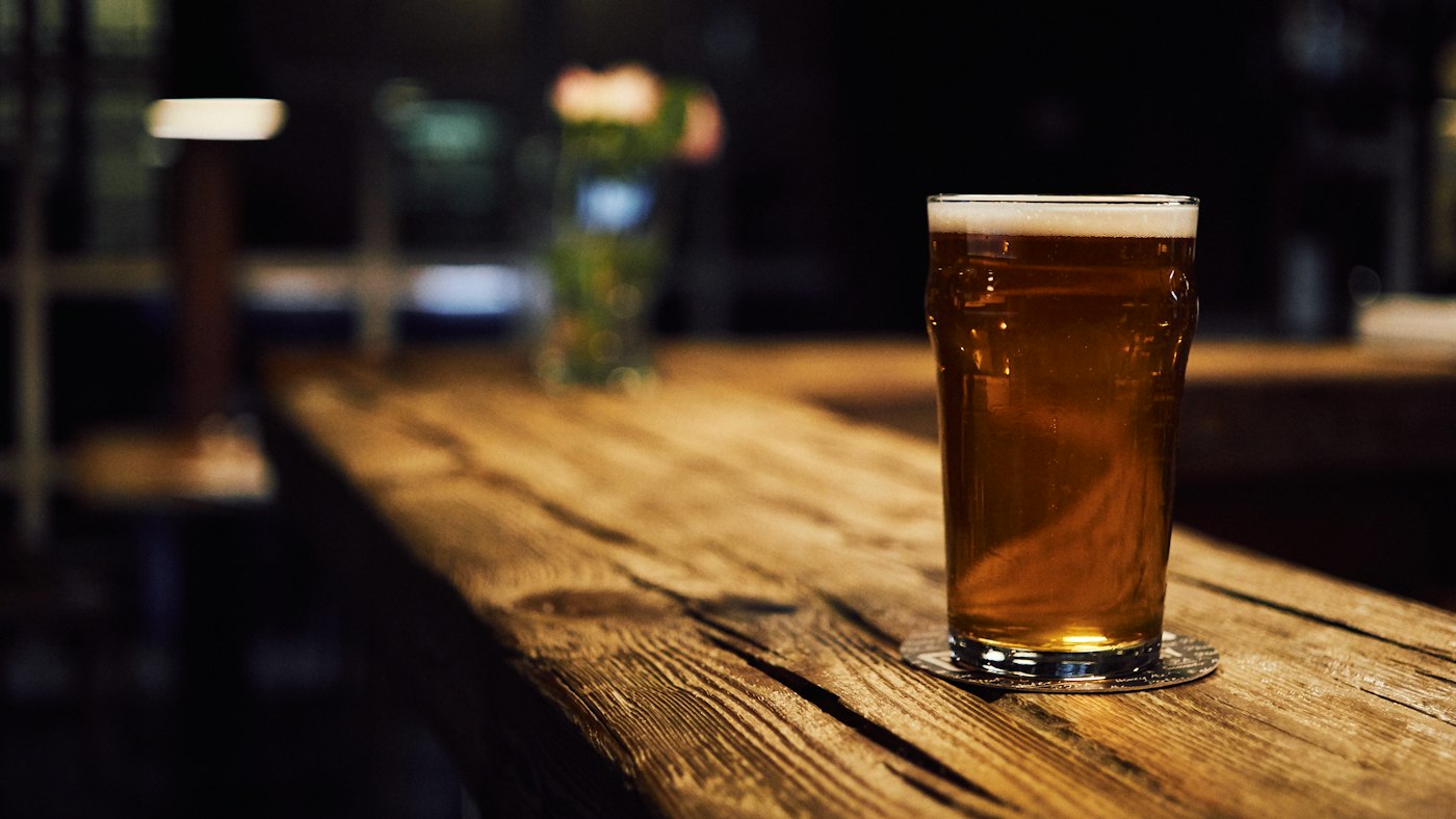 A copper ale in a pint glass on a dark wooden bar