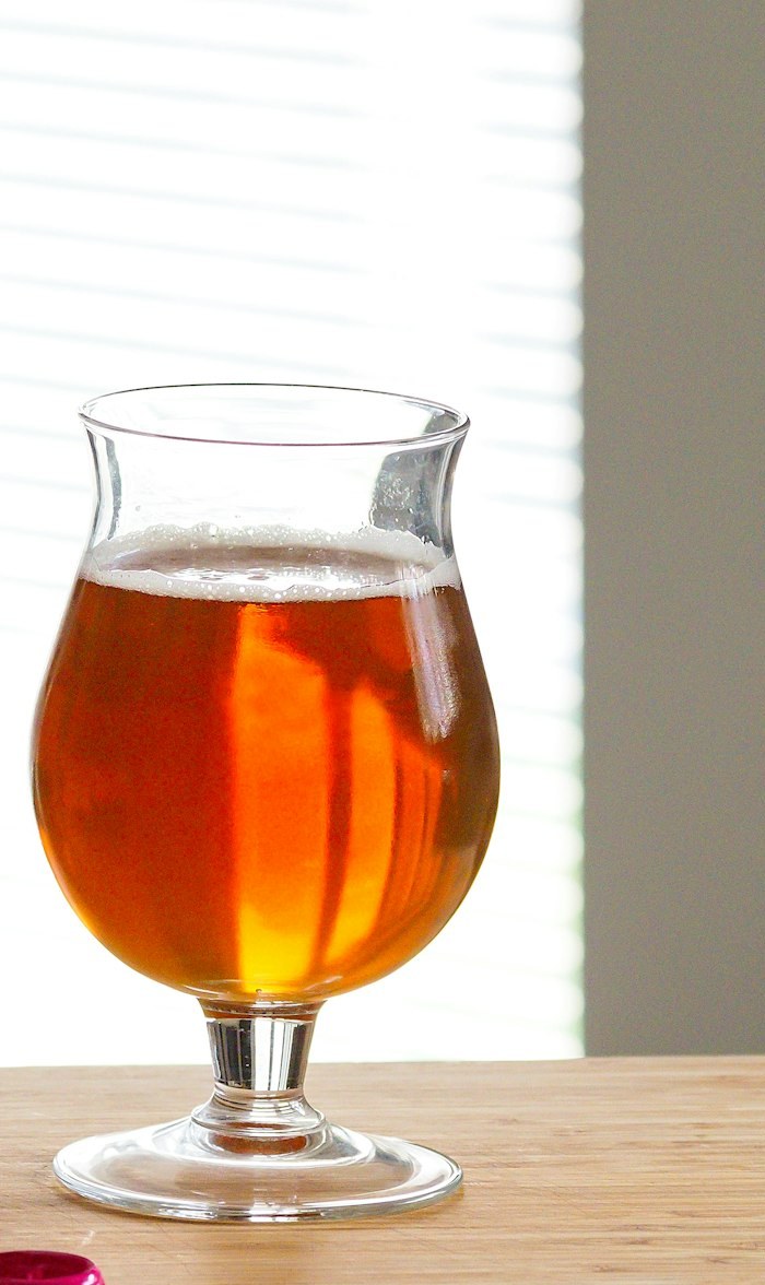 A tulip glass of copper IPA on a pale wood table
