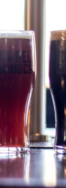 A reddish-brown ale in a pint glass, darker beer beside it